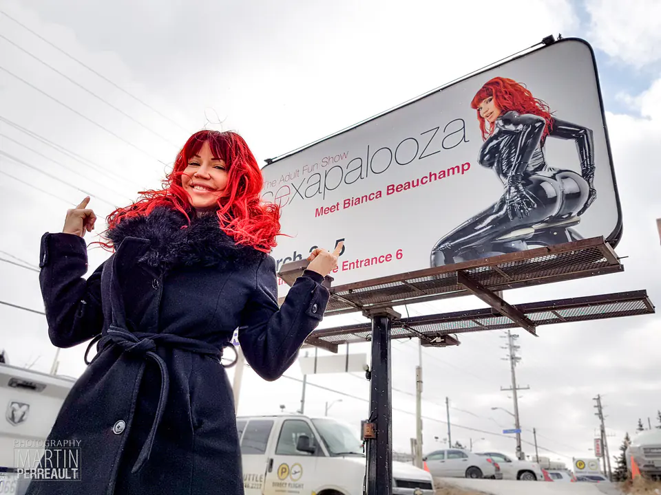 Bianca Beauchamp in a winter coat in front of an event billboard with her photograph, Toronto, 2017