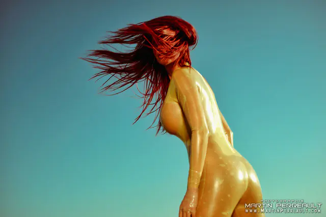 A model in gold, her red hair flying against a teal sky