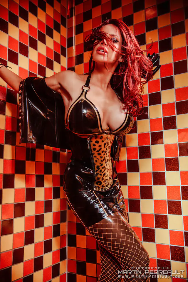 Bianca Beauchamp in black latex and fishnets against a red checkerboard wall