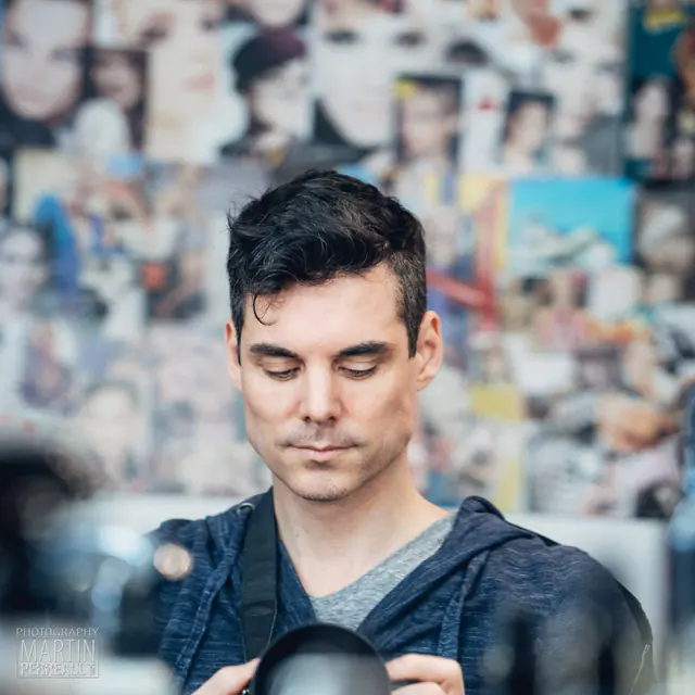 A man holding a camera in front of a wall of photographs