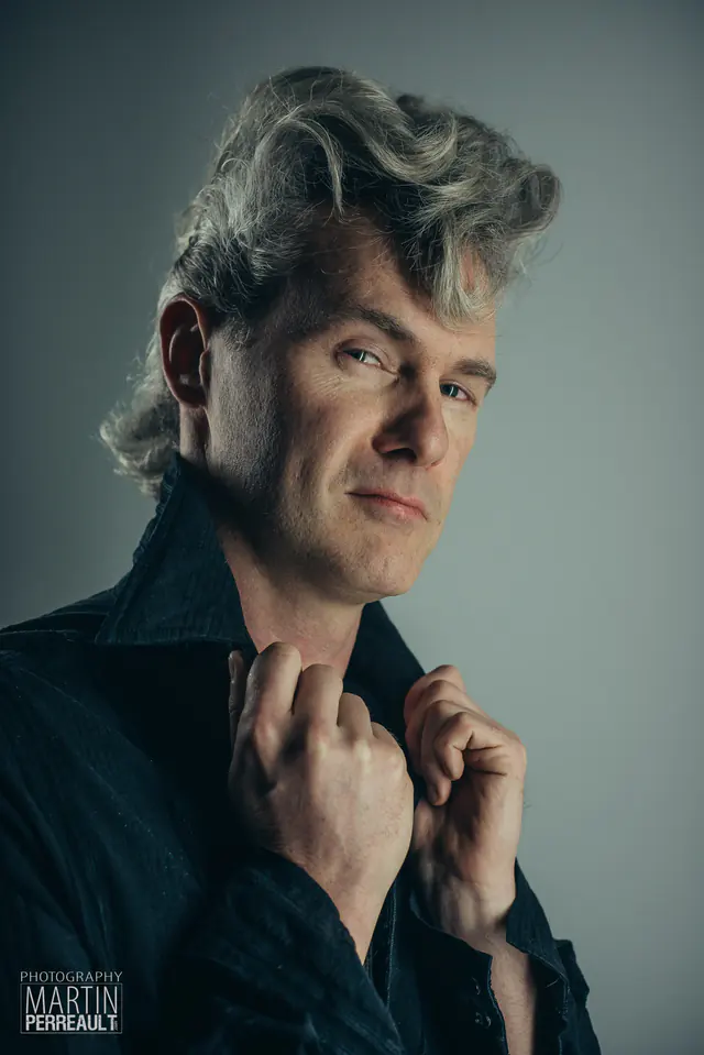 A man with a grey pompadour, holding his collar